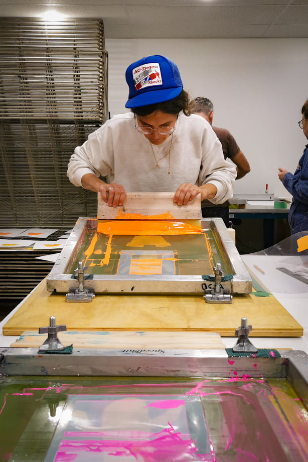 Une artiste applique de l'encre orange à travers une toile de sérigraphie dans un atelier
