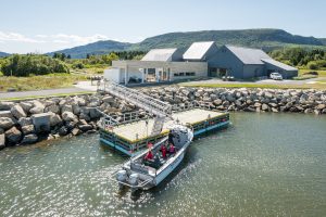 Un bateau quitte le havre de Cap-des-Rosiers avec, en arrière-plan, le centre d'accueil et de découverte. 