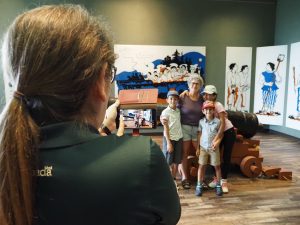Une employée de Parcs Canada prend une photo d'une famille devant un ancien canon. 